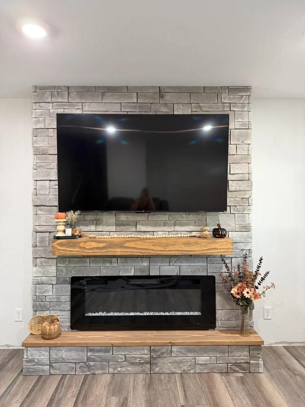 Floor-to-ceiling stone fireplace wall with electric fireplace, wood mantel and mounted TV