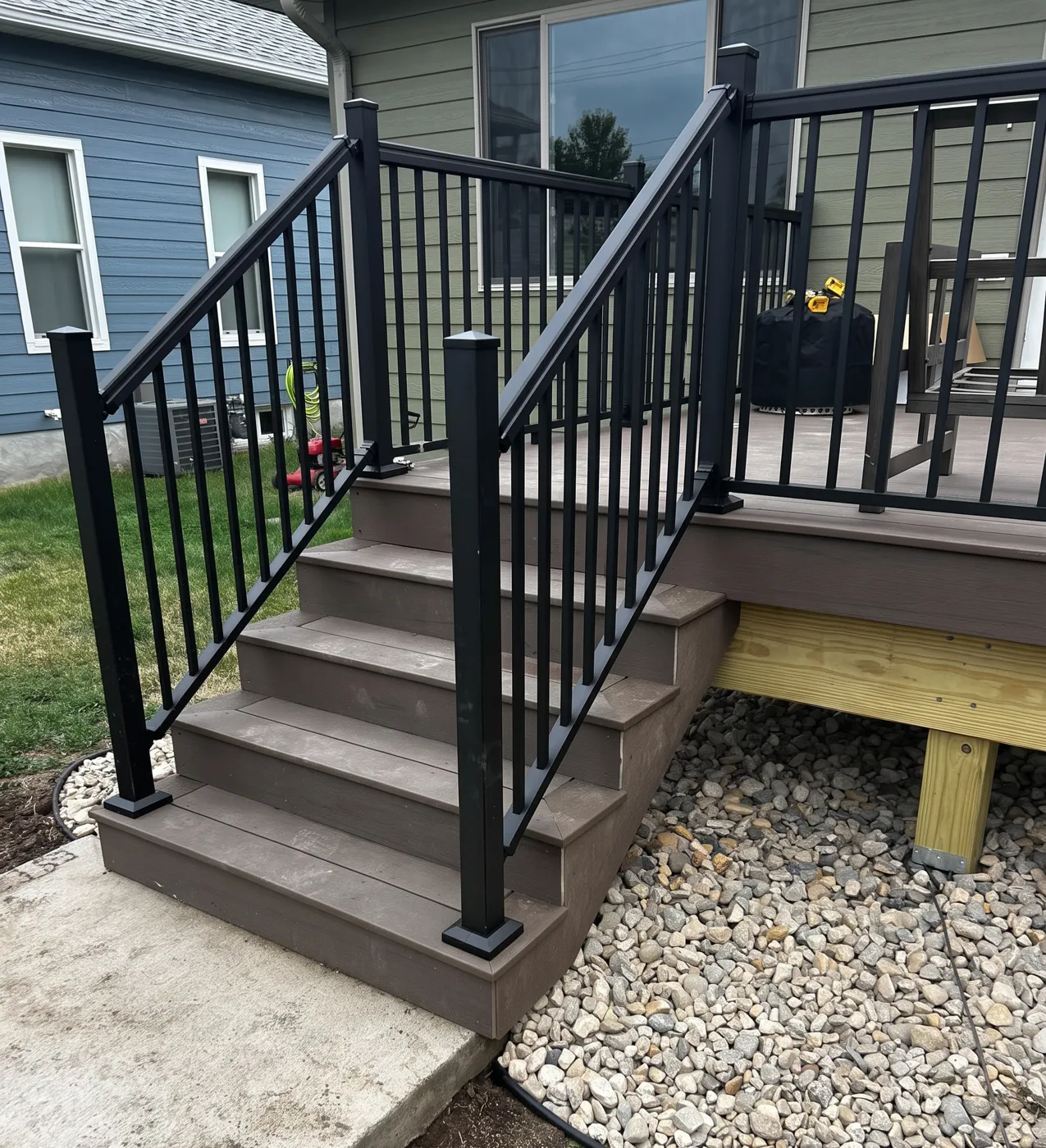 Composite deck stairs with black metal railing and rock landscaping