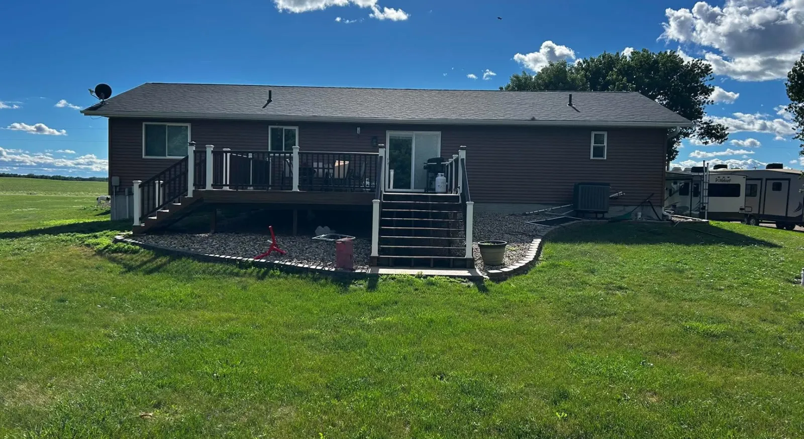 Rear deck with white posts, dark railing and two stairways on a brown-sided ranch home