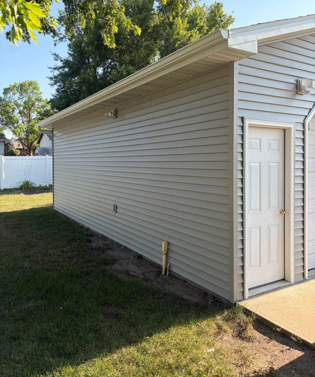 Side of a garage with new vinyl siding, soffit and white service door