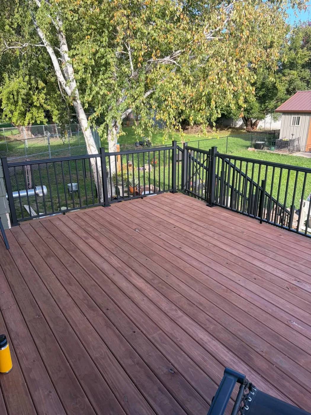 Wood-tone deck boards with black metal railing overlooking a backyard