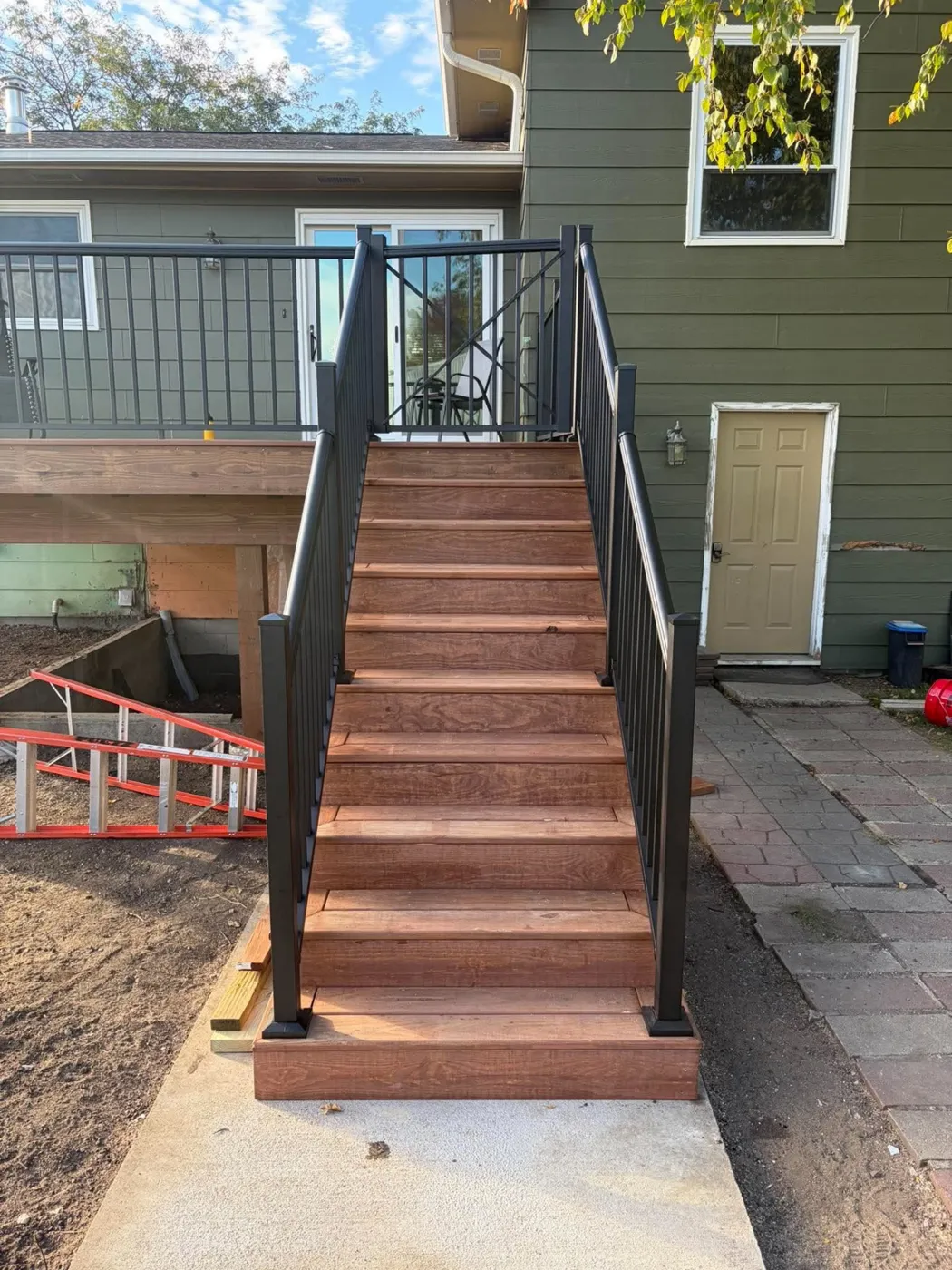 Tall composite deck stairway with black metal railing next to green-sided home